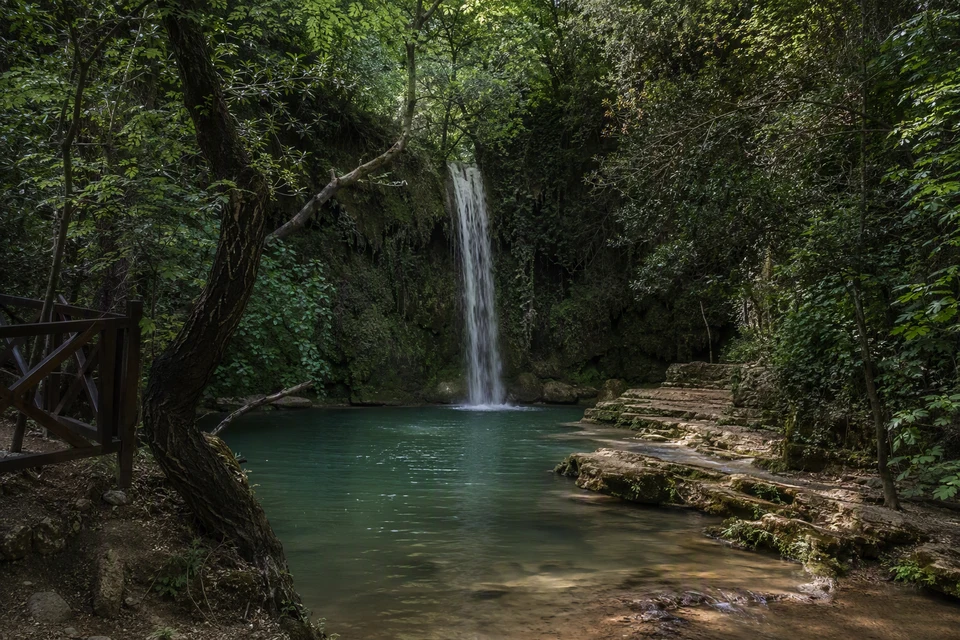 The main Kursunlu Waterfall dropping into a jade-green pool in a wooded ravine, AI recreation
